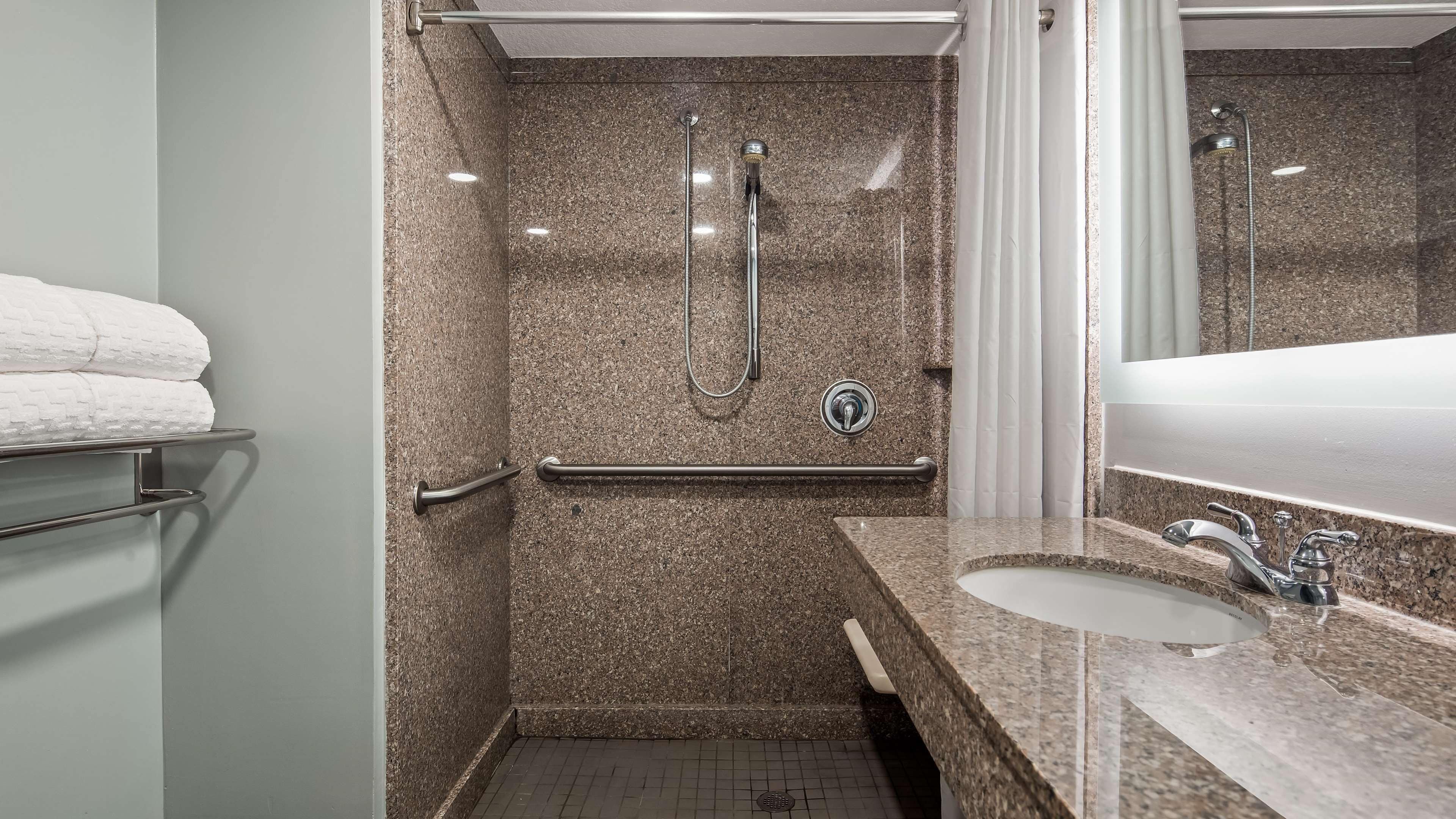 A bathroom with a granite shower, a grab bar, a sink, and a mirror.