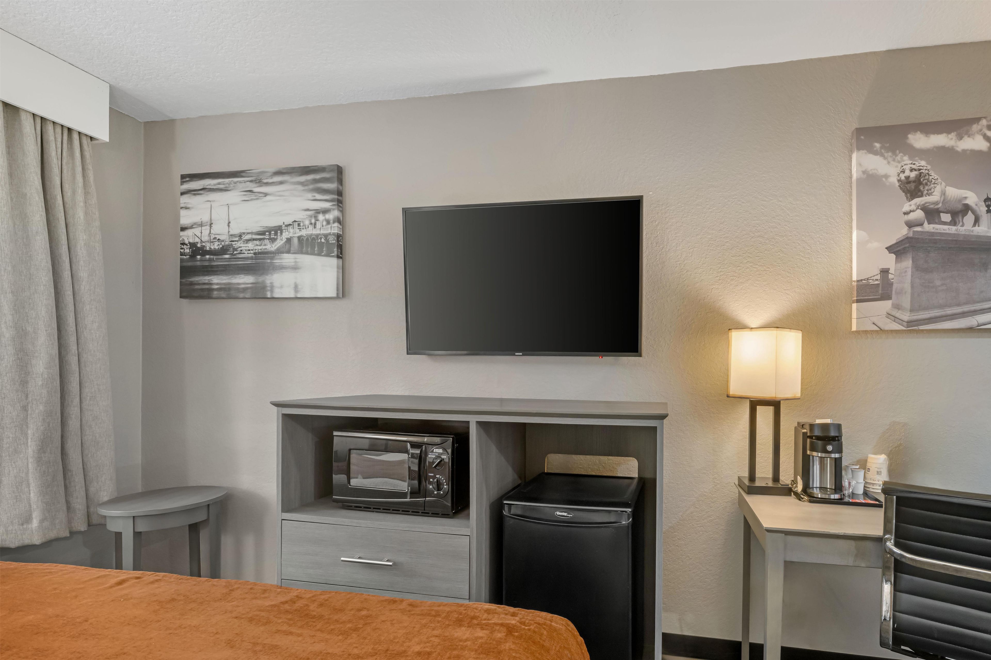 A hotel room with a bed, a desk with a microwave, a coffee maker, and a TV on the wall.