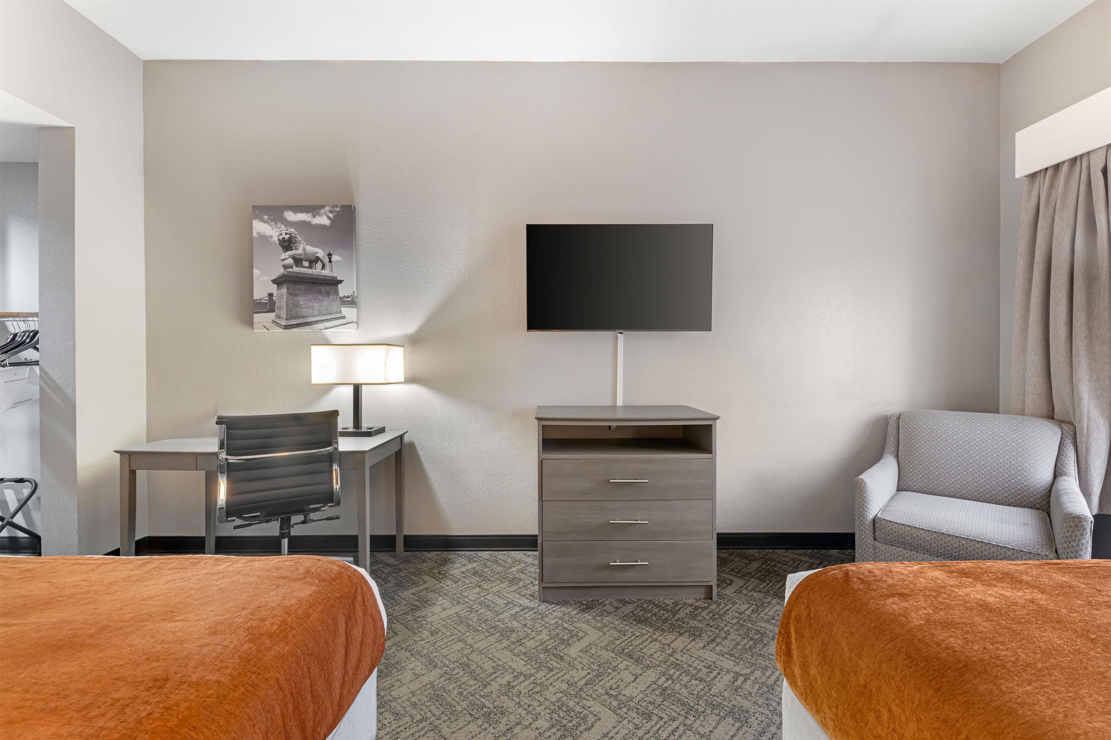 A hotel room with two beds, a desk, a chair, a TV, a lamp, and a wardrobe.