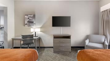 A hotel room with two beds, a desk, a chair, a TV, a lamp, and a wardrobe.