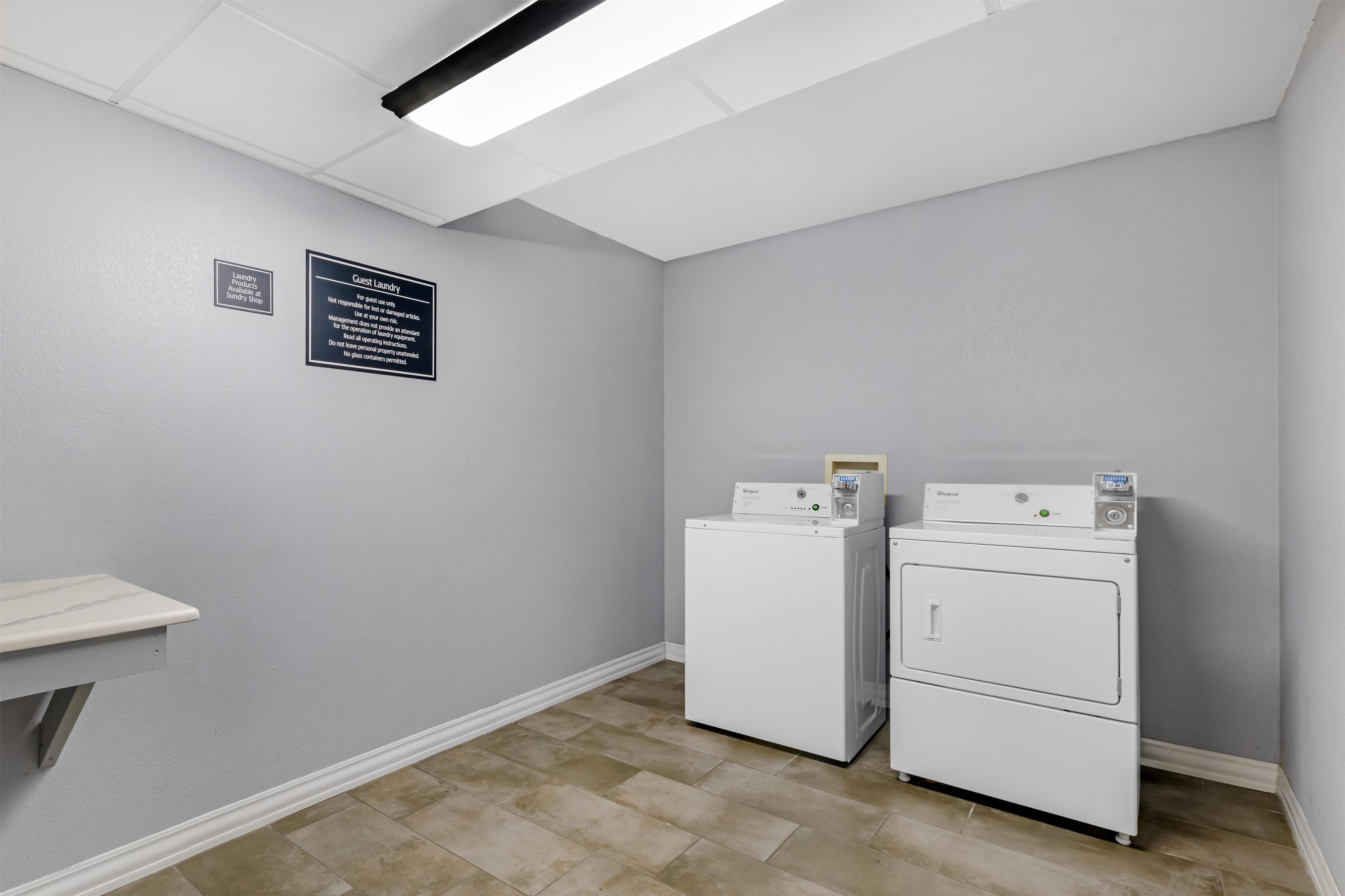 A laundry room with two Whirlpool washers and dryers, a sign indicating guest laundry use, and a shelf with laundry products.