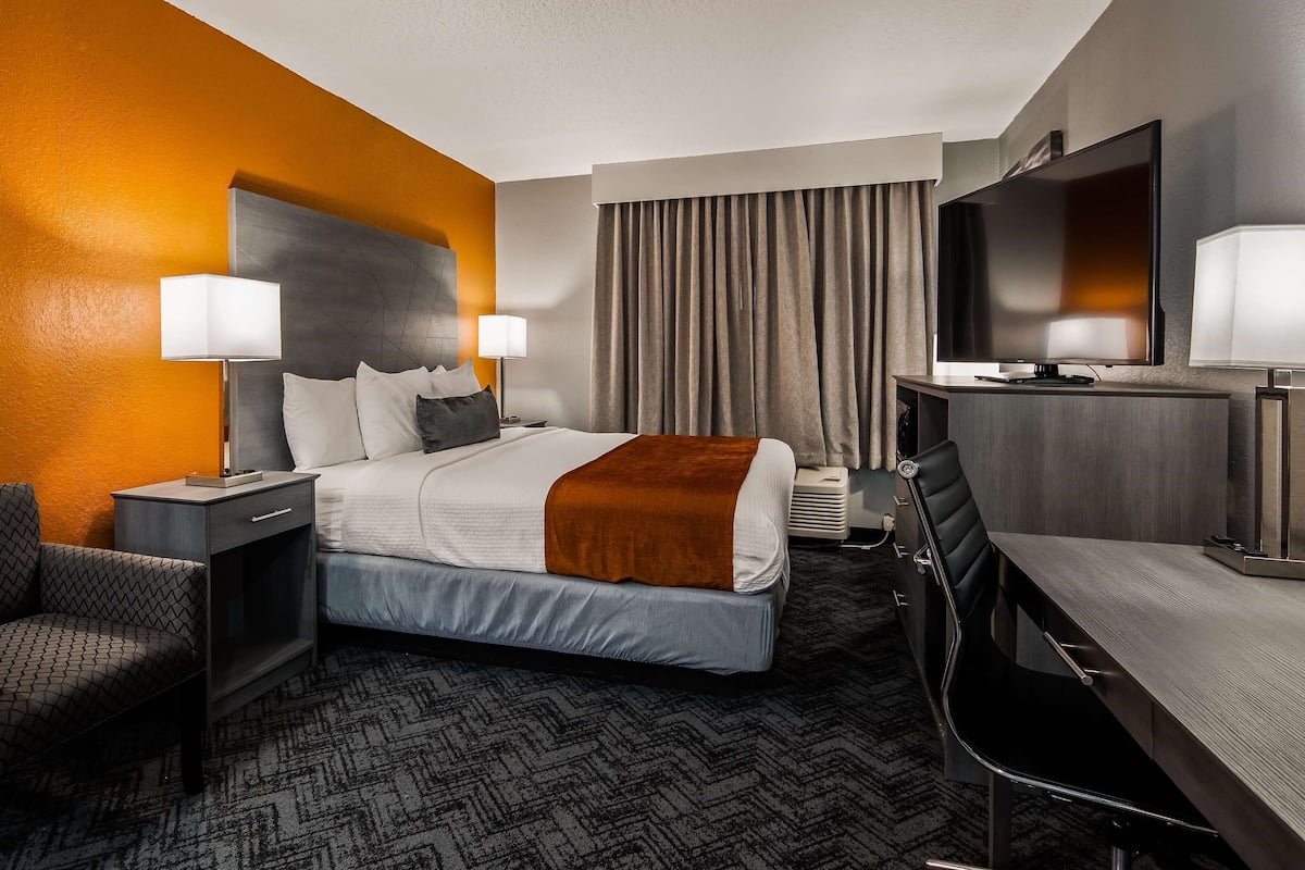 A hotel room with a bed, a desk, a chair, a TV, and a window with curtains.