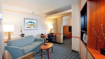 Une chambre d’hôtel avec un canapé, une petite table, un bureau avec une chaise, une télévision et une armoire en bois.