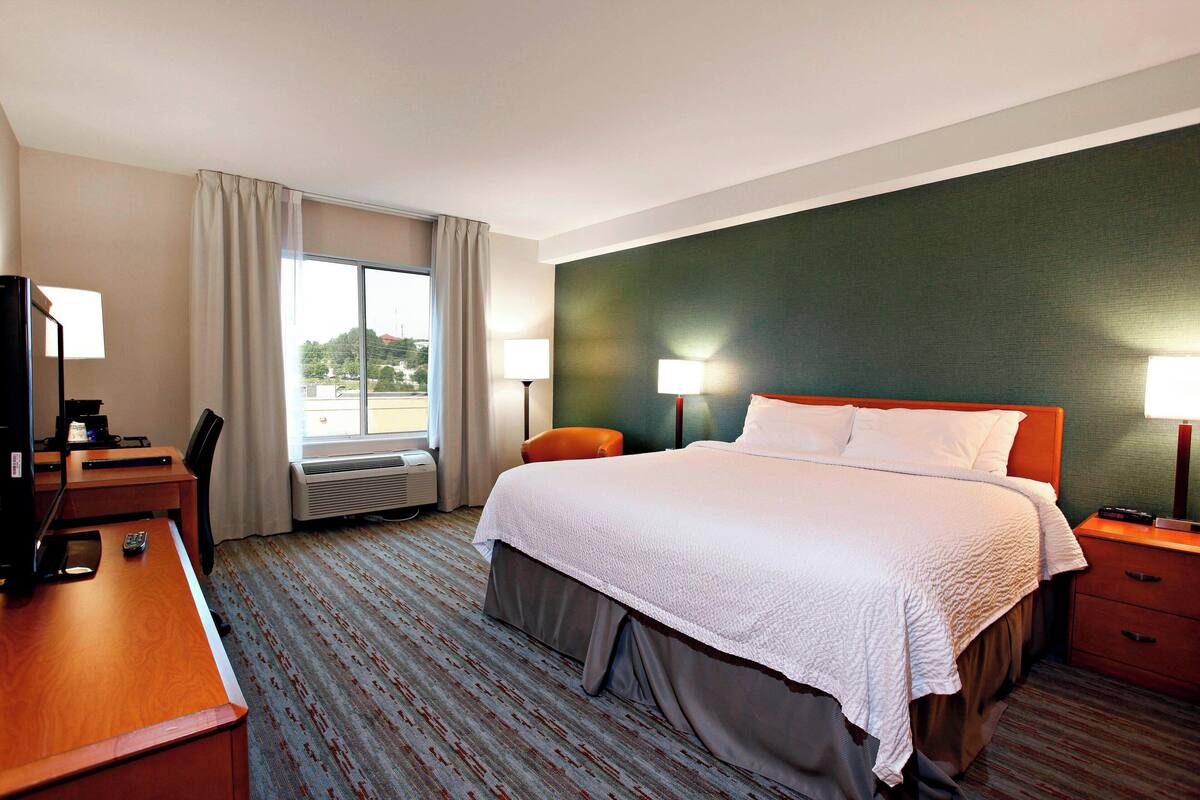 Een hotelkamer met een groot bed, een bureau met een computer, een stoel, twee bedlampen en een raam met gordijnen.
