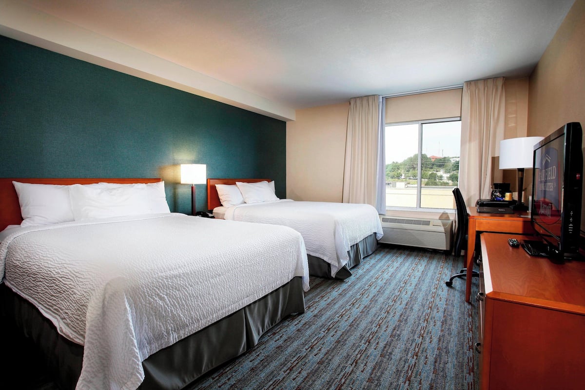 Een hotelkamer met twee bedden, een bureau met een televisie en een raam met gordijnen.