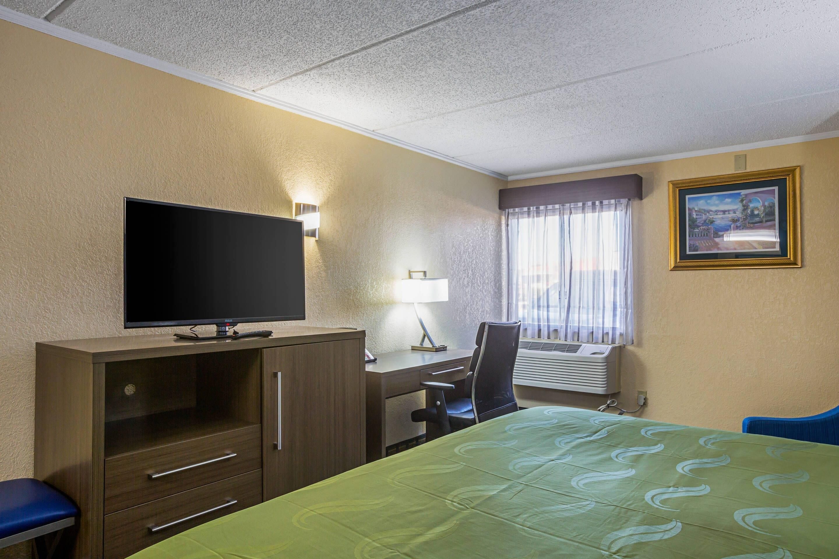 A hotel room with a bed, a desk, a chair, a television, and a window with curtains.