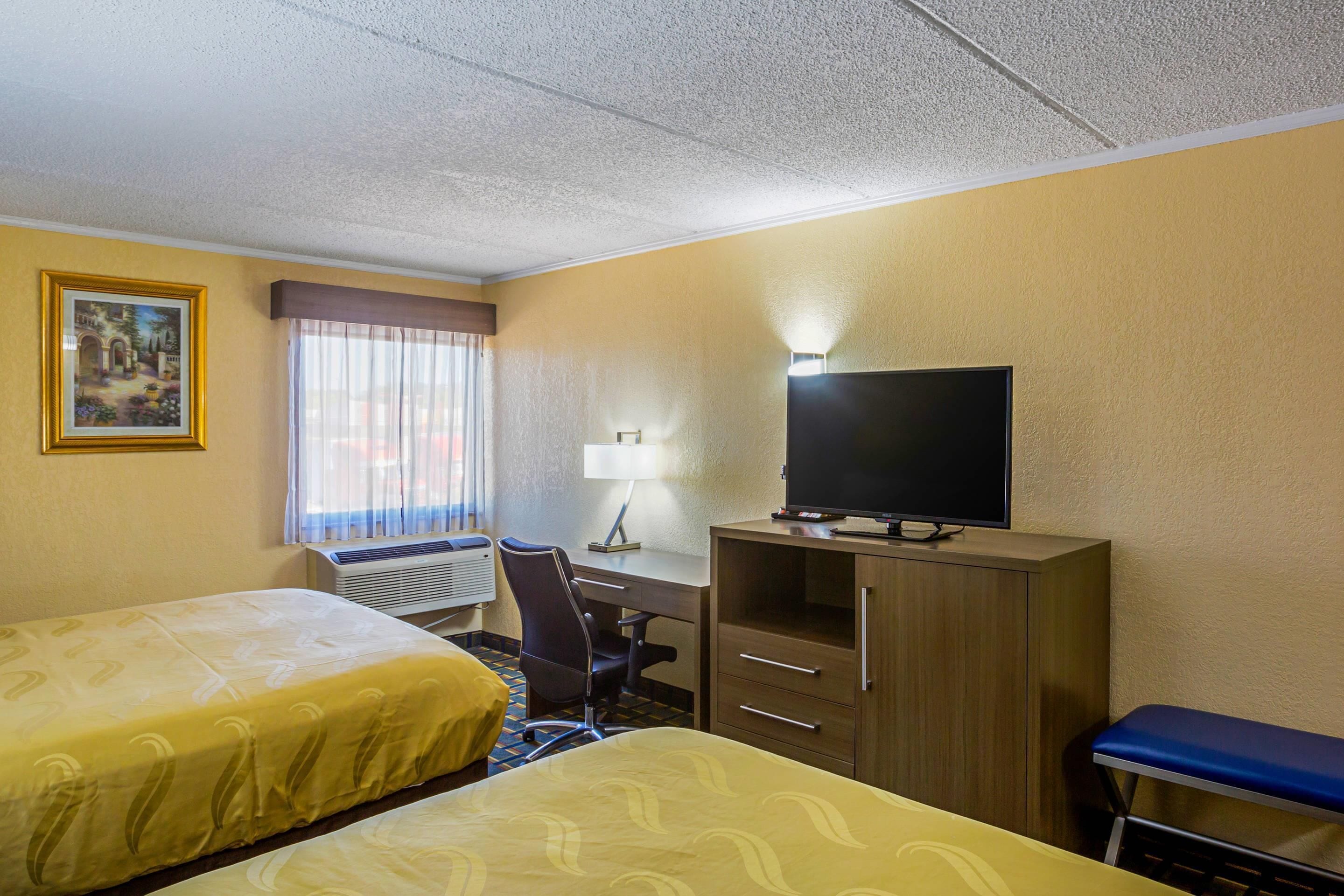 A hotel room with two beds, a desk with a television, a chair, and a window with curtains.