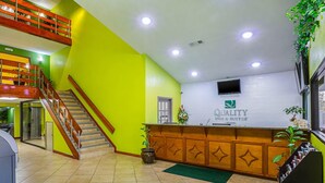 A hotel reception area with a green wall, a wooden reception desk, a staircase, and a potted plant. - Quality Inn & Suites near Six Flags East (Atlanta)