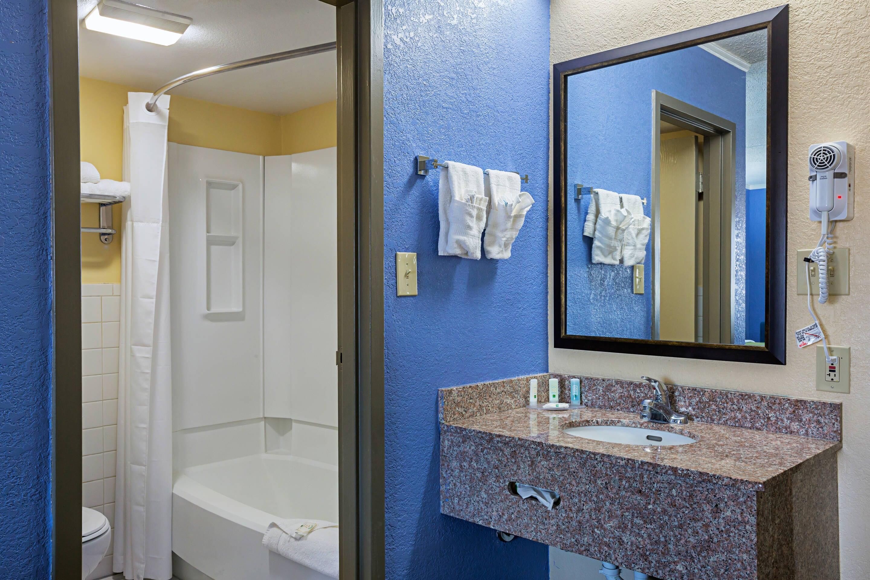 A bathroom with a bathtub, a sink with a mirror, and a hairdryer on the wall.
