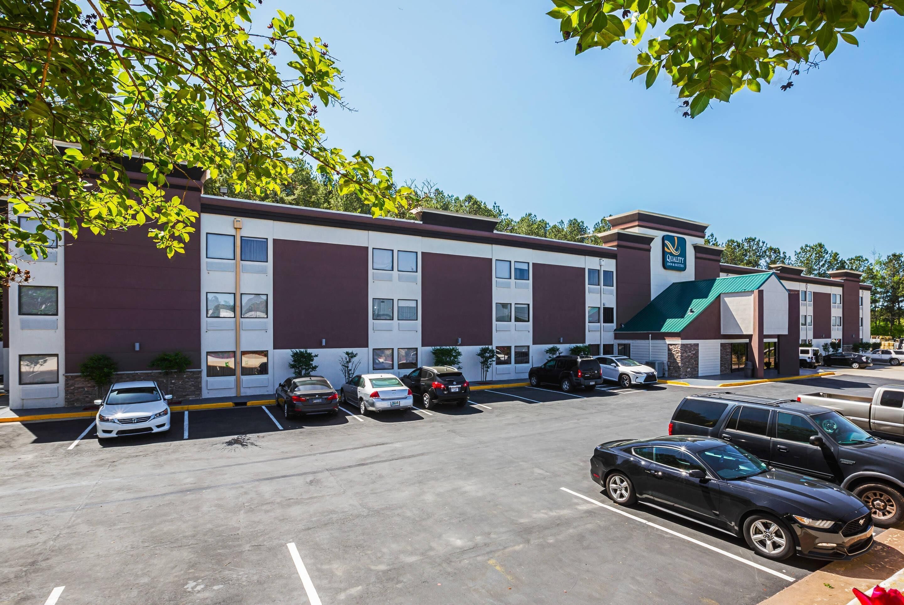 A hotel with a parking lot, several cars, and a building with a green roof and a sign that says "Quality Inn".