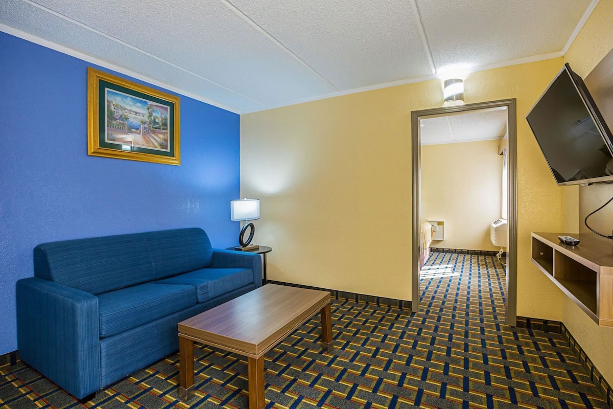 A hotel room with a blue sofa, a small table, a lamp, a TV, and a patterned floor.