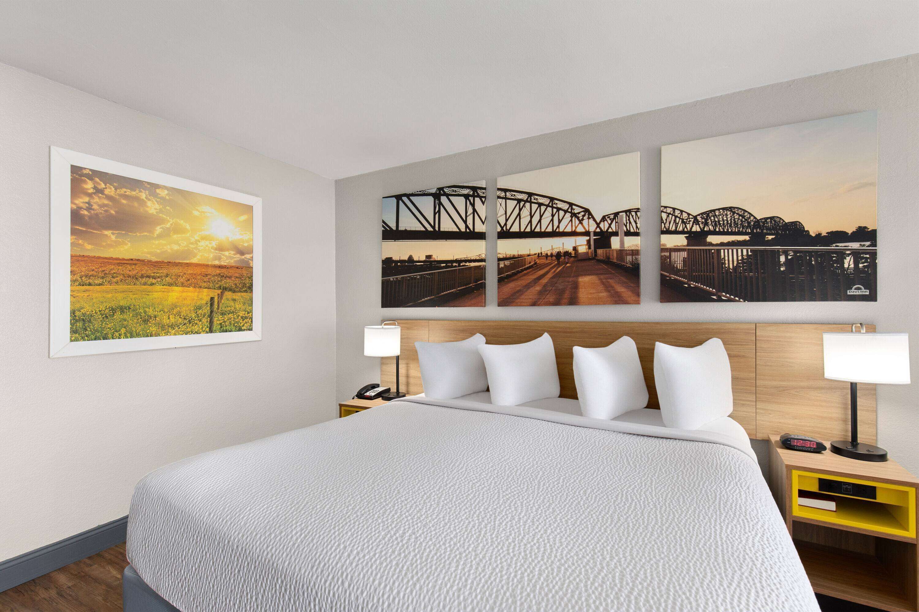 A hotel room with a large bed, two bedside tables, a nightstand, and three framed photographs on the wall.