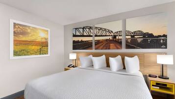 A hotel room with a large bed, two bedside tables, a nightstand, and three framed photographs on the wall.