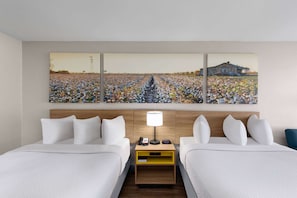 A hotel room with two beds, a nightstand with a lamp, and a large painting of a field and barn on the wall. - Days Inn by Wyndham Carlisle (Carlisle)