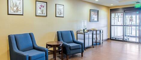 A waiting area with two blue armchairs, a small table, and framed artwork on the wall.