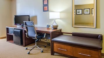 A hotel room with a desk, chair, TV, lamp, and a sofa.