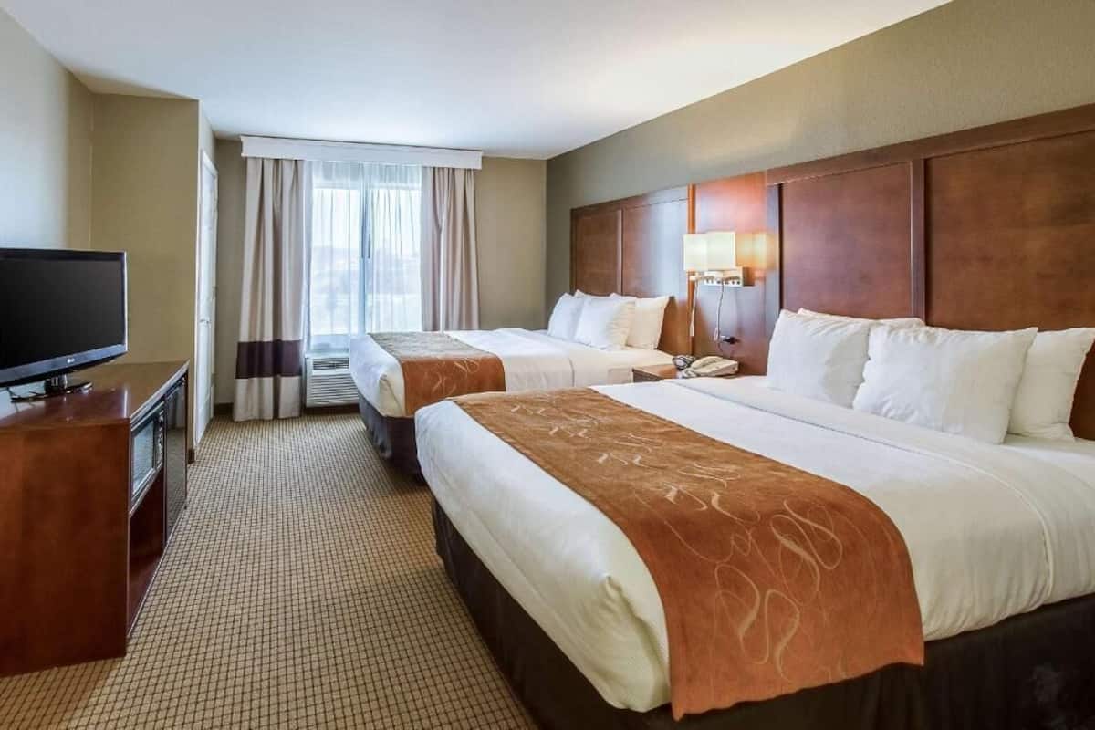 Ein Hotelzimmer mit zwei Betten, einem Schreibtisch, einem Fernseher und einem fensterbepflanzten Fenster.