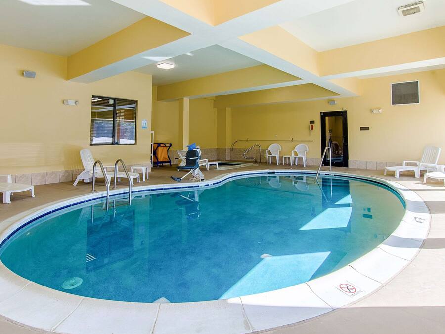 An indoor swimming pool with clear blue water, surrounded by white lounge chairs and a tiled deck.