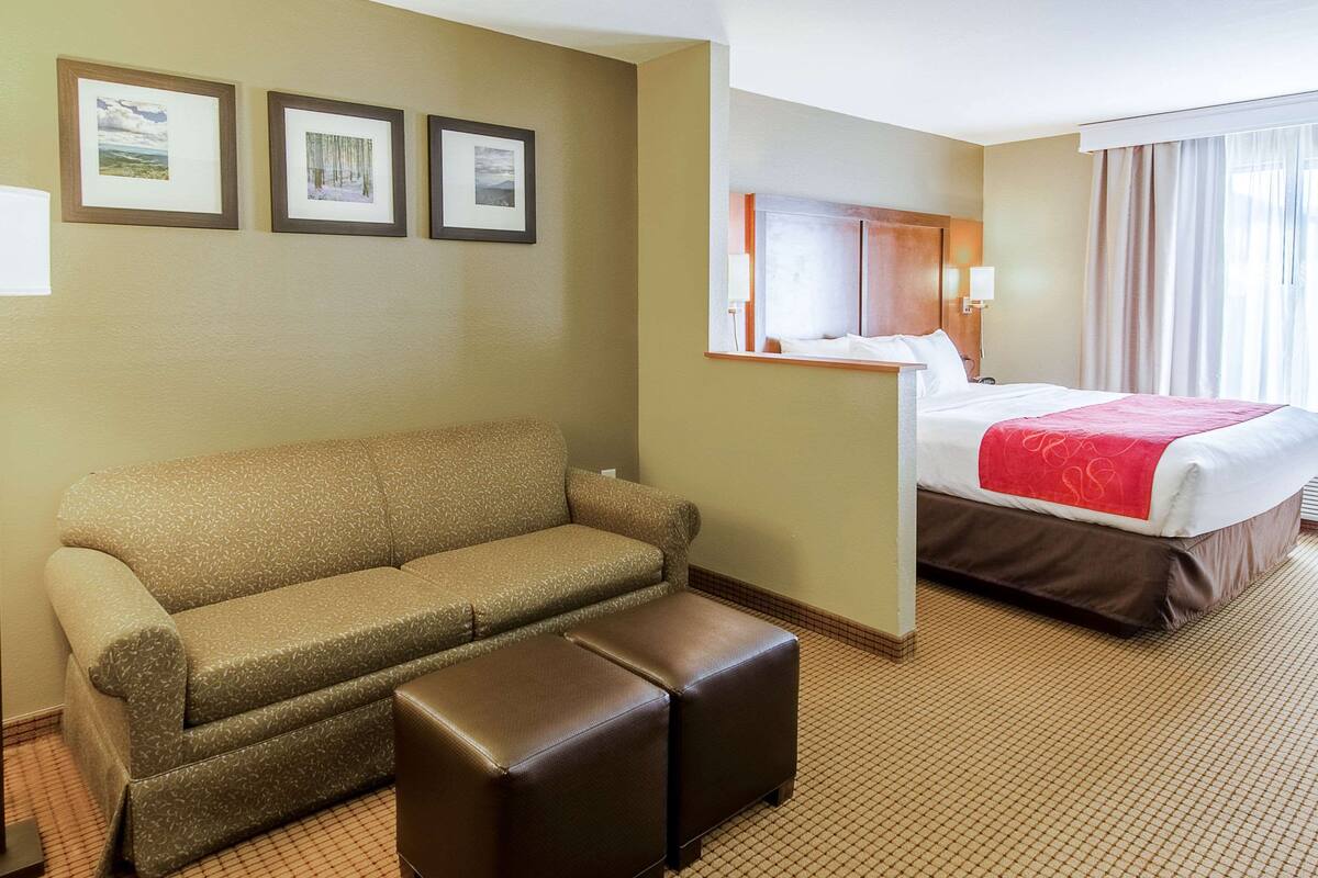 Ein Hotelzimmer mit einem Bett, einem Schlafsofa, einem Hocker und drei gerahmten Bildern an der Wand.