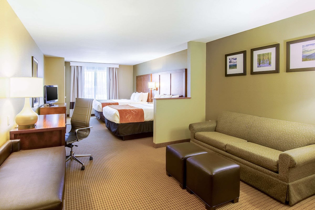Ein Hotelzimmer mit Bett, einer Couch, einem Schreibtisch mit Lampe, einem Sessel und einem Fernseher.