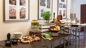 Une table de buffet garnie de divers plats, un distributeur d’eau et un tableau représentant des bâtiments accroché au mur.