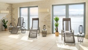 Un balcon spacieux offrant une vue sur la mer, aménagé avec des chaises et des tables modernes, et agrémenté de plantes en pot.