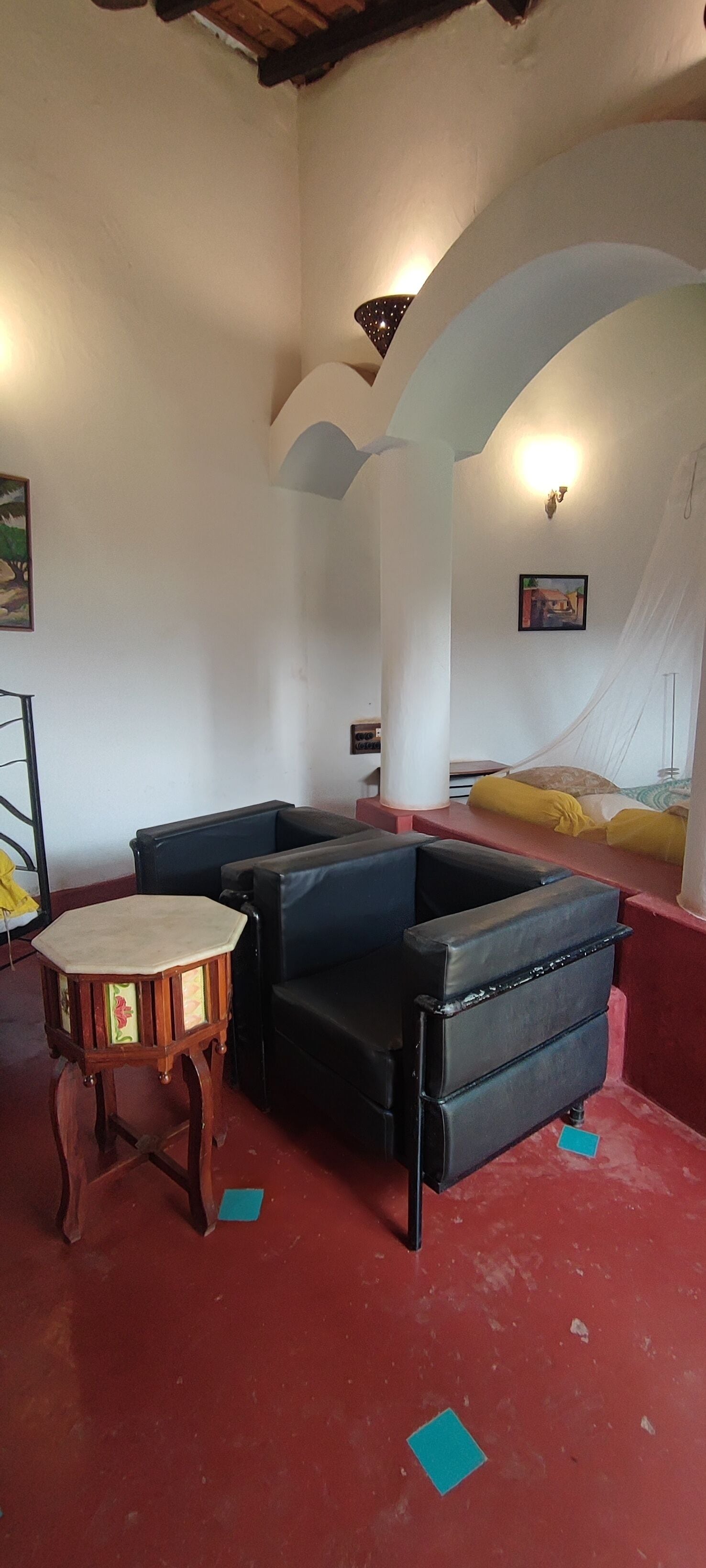 Ein Zimmer mit rotem Boden, einem runden Tisch, einer Couch und einem Himmelbett.