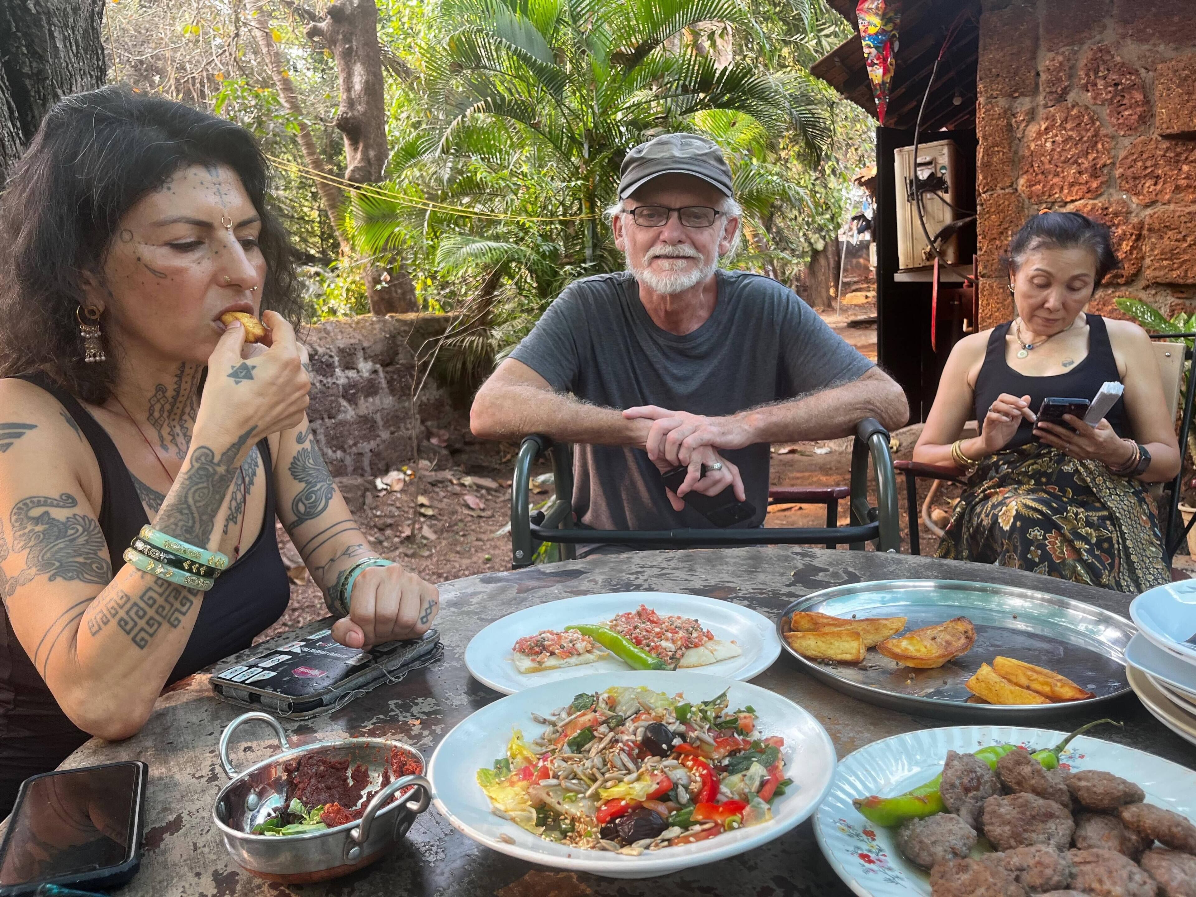 Un grupo de personas sentadas en una mesa al aire libre, con varios platos, incluyendo ensaladas y comida a la parrilla.