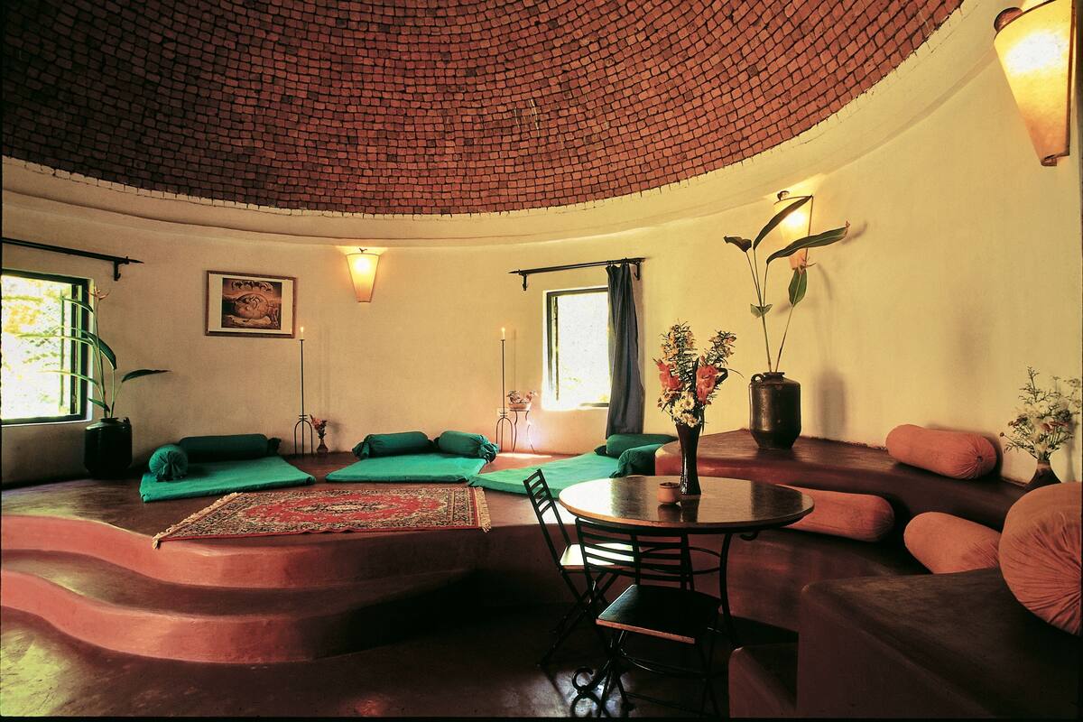 A cozy living room with a curved ceiling, green cushions, a round table, and a vase with flowers.