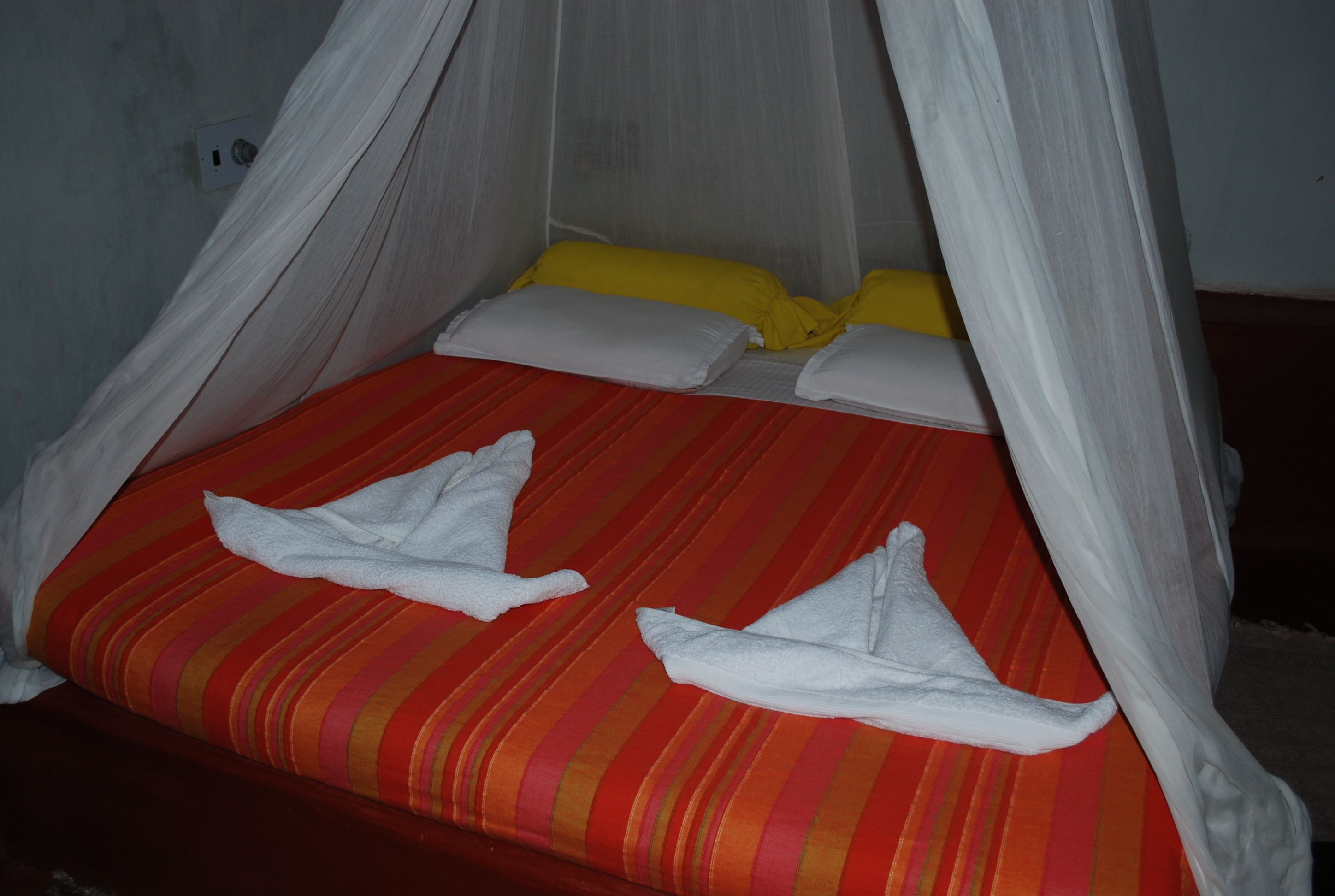 Una cama con una colcha a rayas rojas y naranjas, almohadas blancas y un dosel.