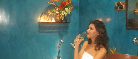A person sitting in a bathtub with a towel wrapped around their body, a sink, and a mirror in the background.