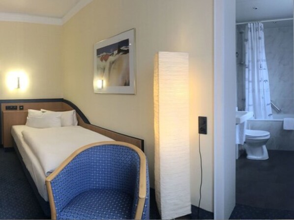 Een hotelkamer met een bed, een stoel, een schilderij aan de muur en een badkamer met toilet en douche.