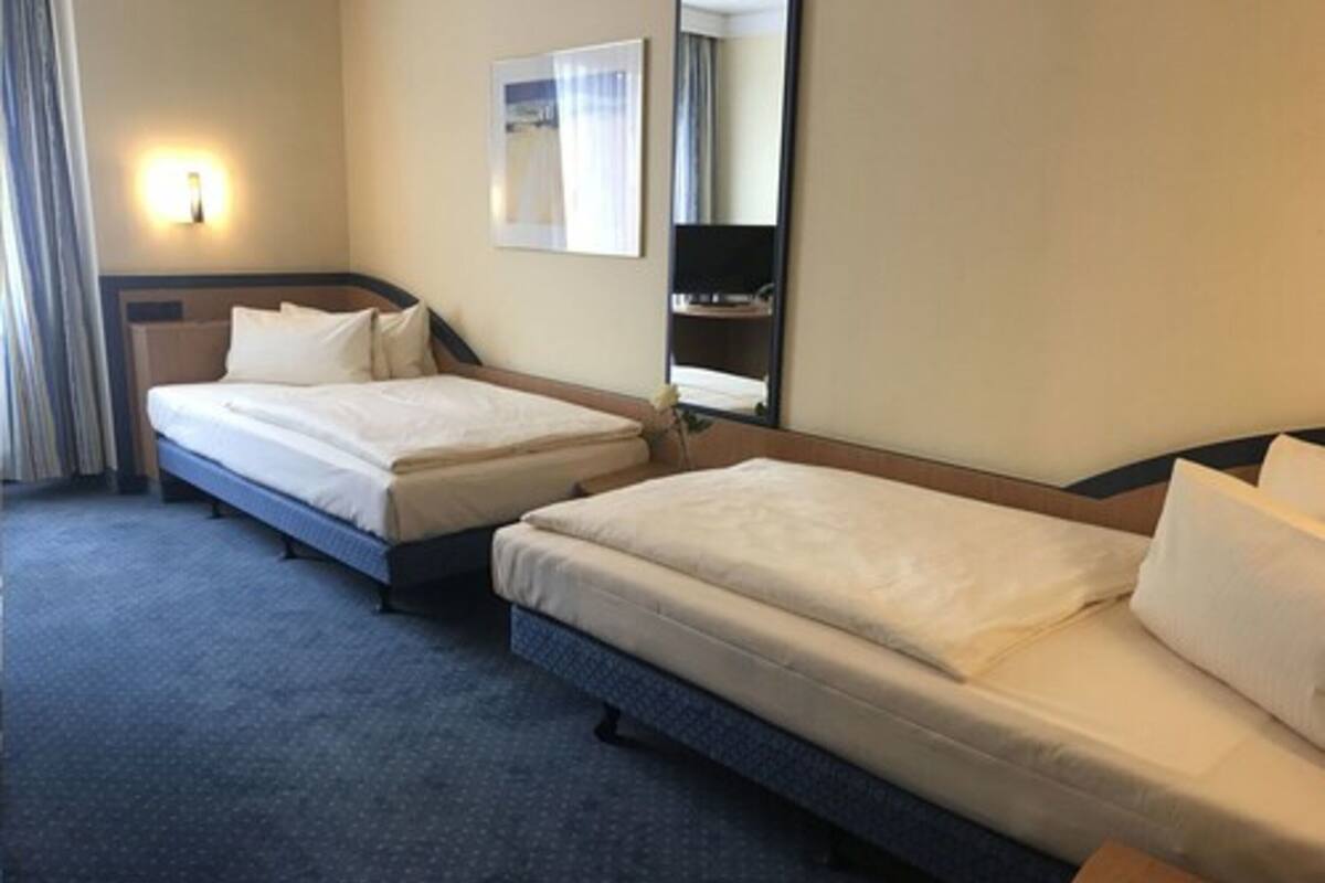Una habitación de hotel con dos camas, un espejo grande y una lámpara fijada a la pared.