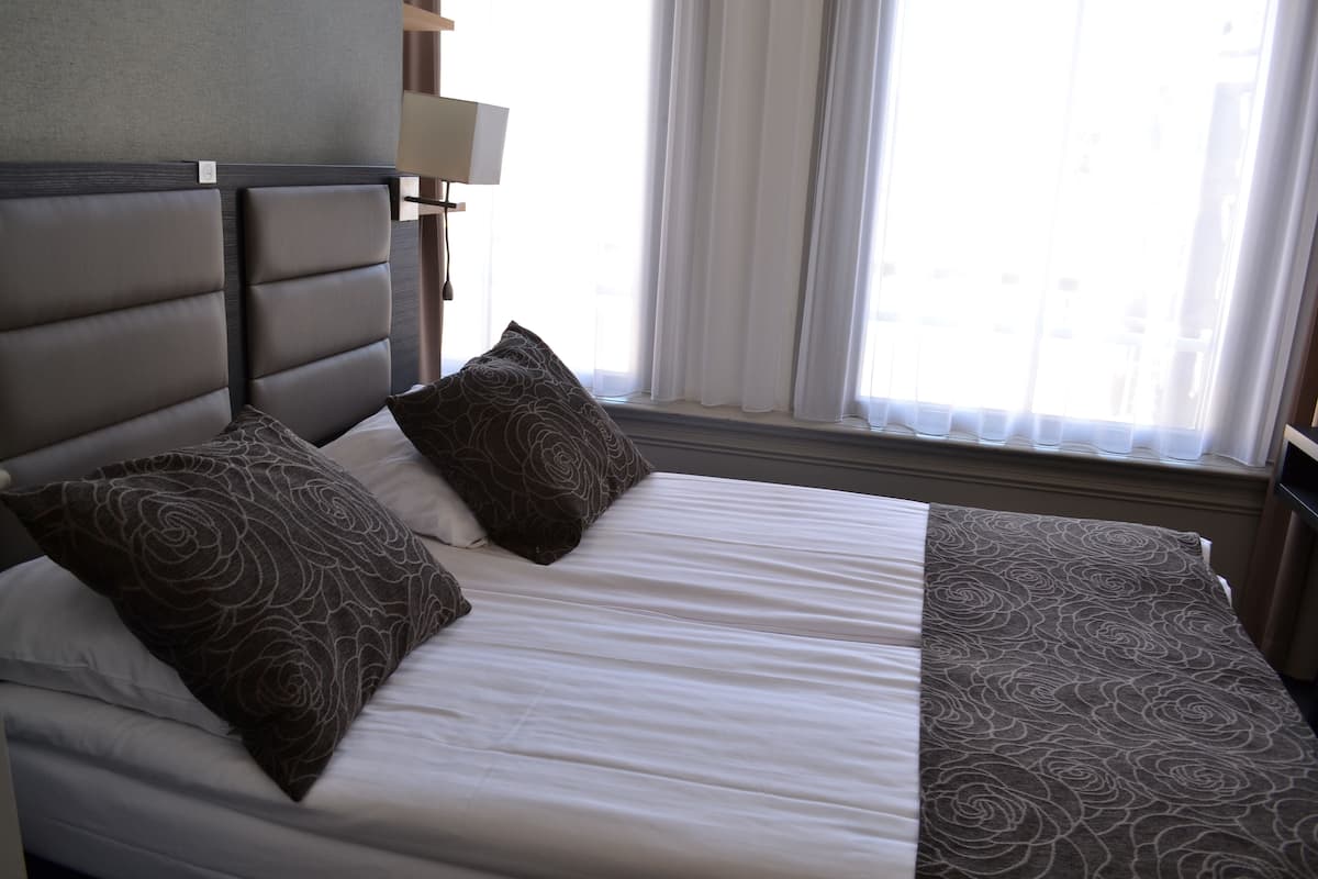 A neatly made bed with a headboard, two pillows, and a blanket.