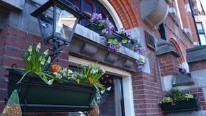A building with a brick facade, a green hanging planter with flowers, and a hanging lantern. - Hotel Clemens Amsterdam (Amsterdam)