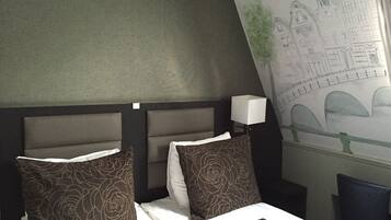 Une chambre d’hôtel avec un lit, deux oreillers, une télécommande et une fresque murale représentant un paysage urbain.