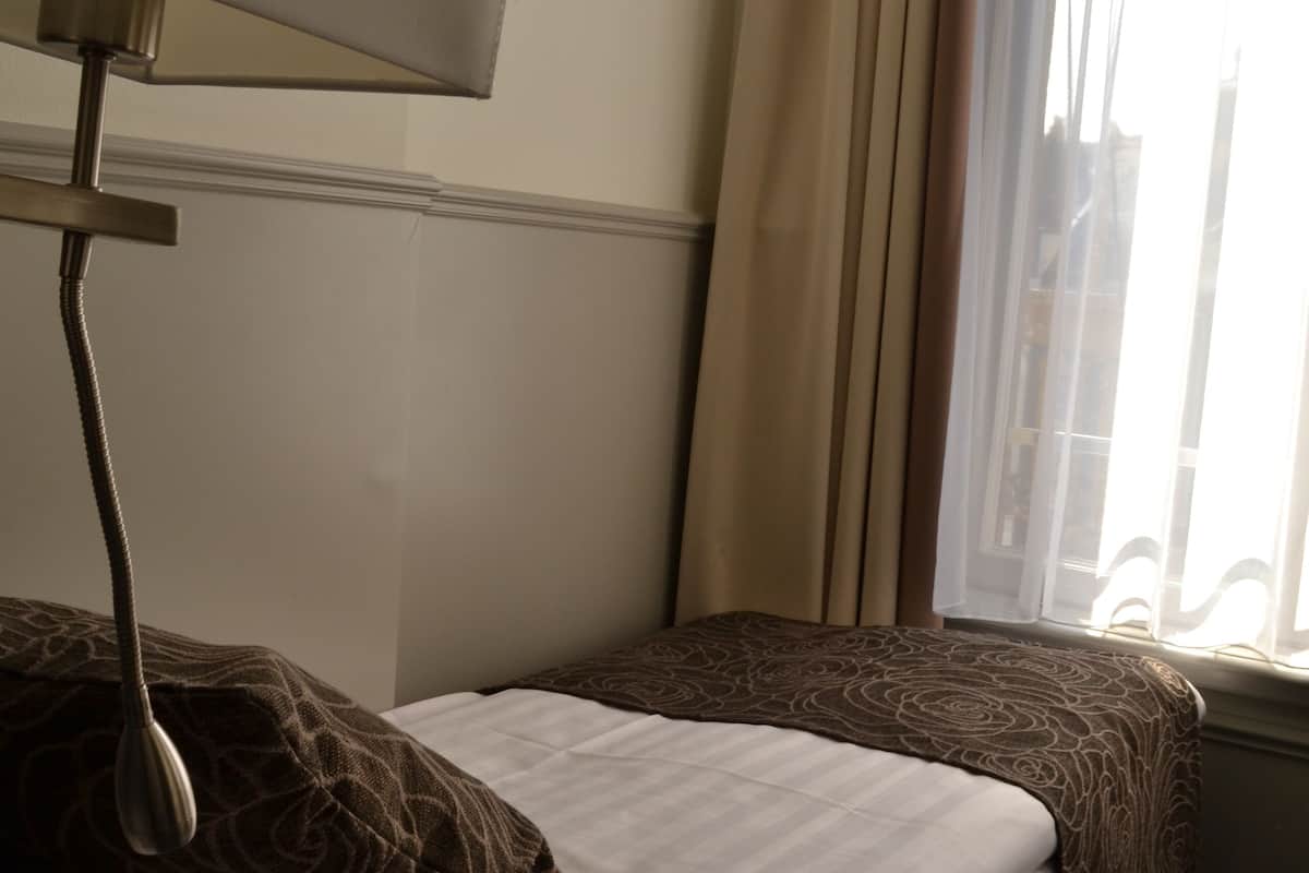 A hotel room with a bed, a lamp, and a window with curtains.