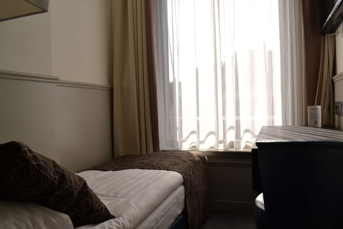 A hotel room with a bed, a small table, and a window with curtains.