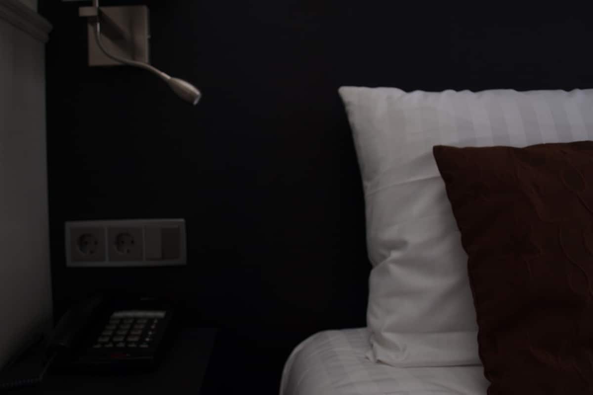 A dark room with a bed, a bedside lamp, and a telephone.