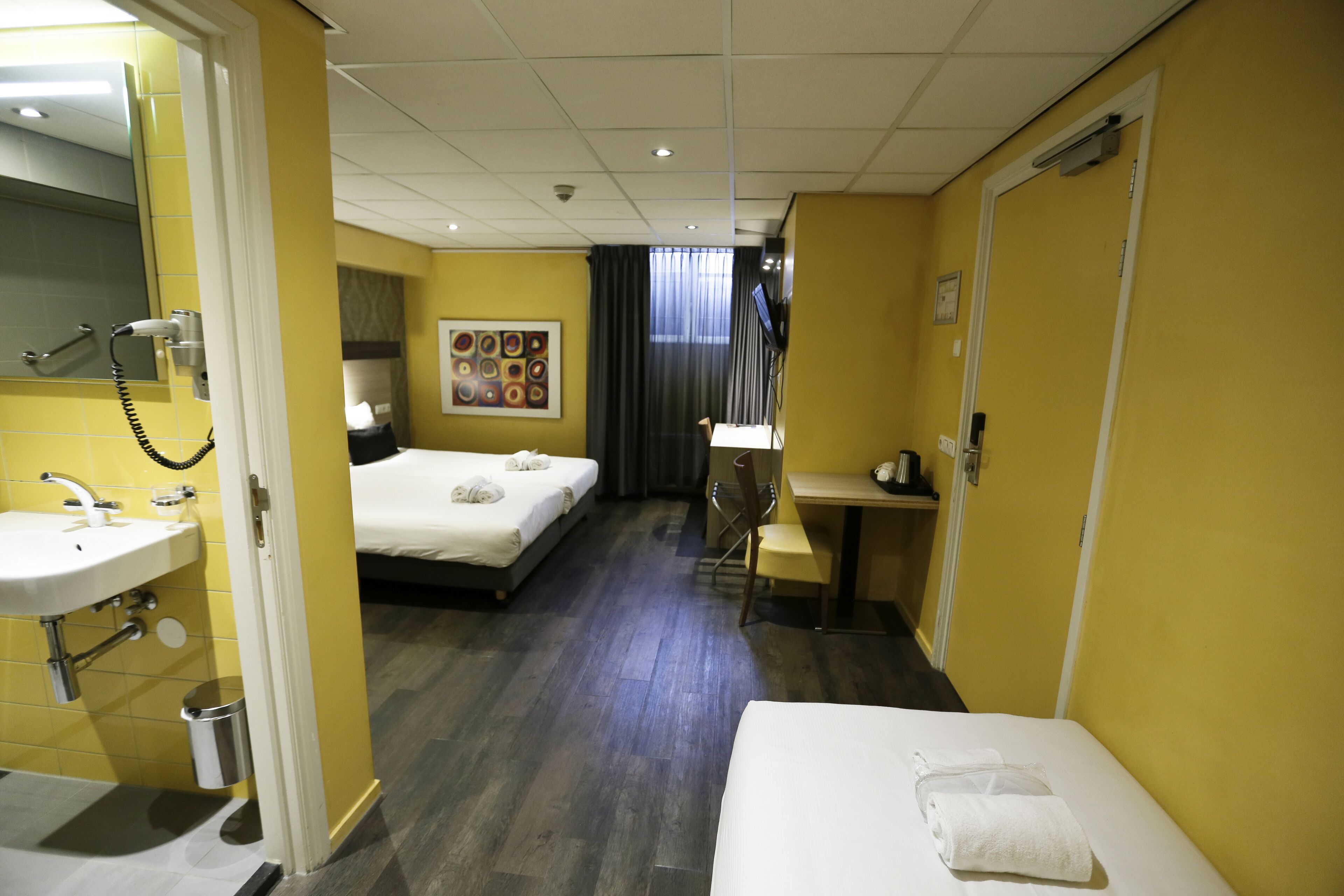 Een hotelkamer met een bed, een bureau, een stoel, een wastafel en een spiegel.