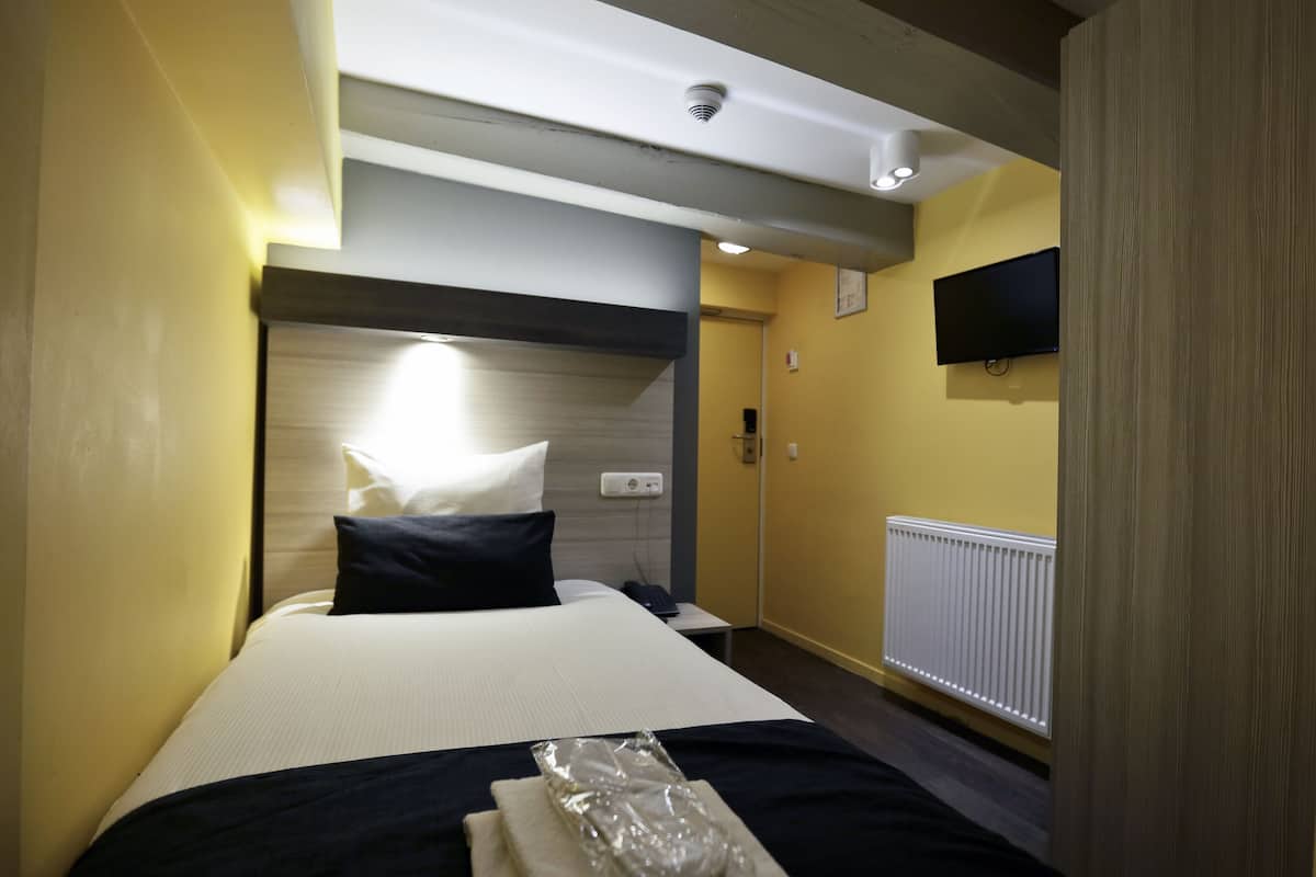 Una habitación de hotel con cama, mesita de noche, televisor montado en la pared y ventana.