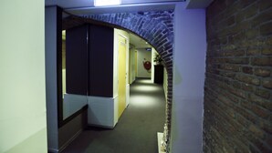 Un estrecho pasillo con un arco de ladrillo, que conduce a una habitación con una puerta blanca y un objeto circular rojo en la pared.