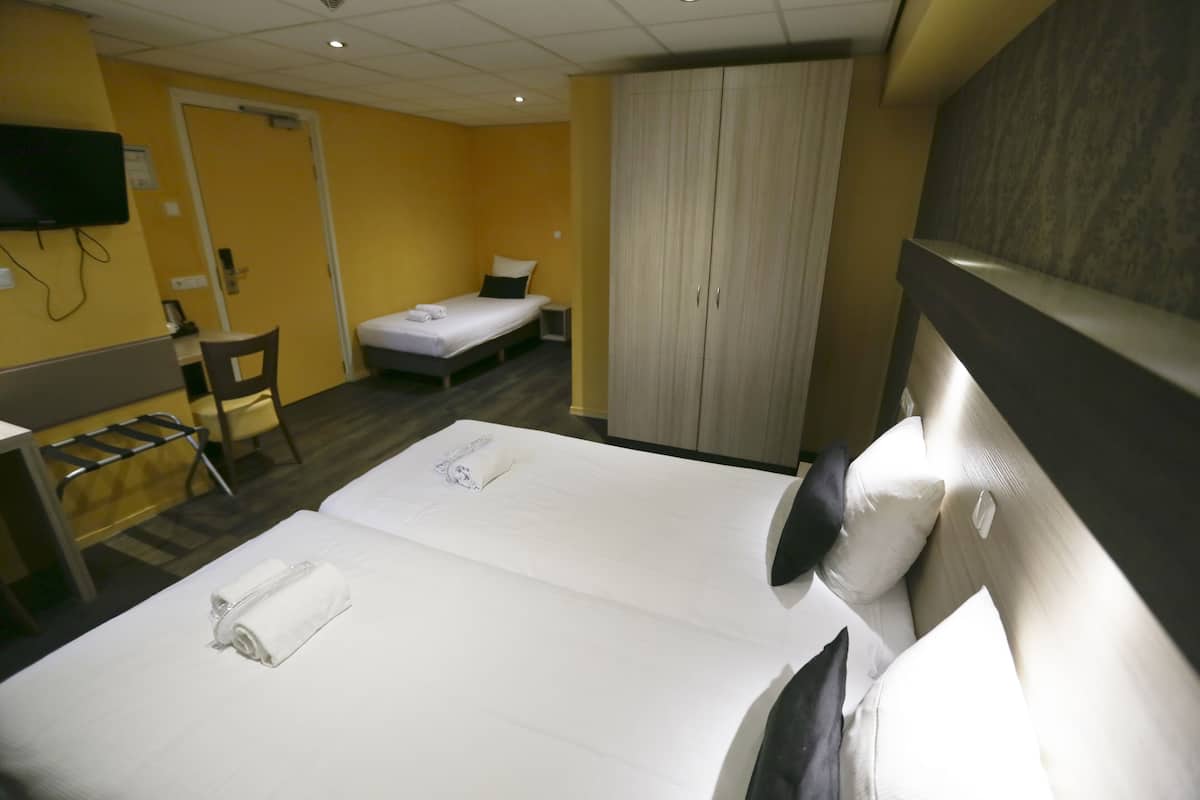 Habitación de hotel con dos camas, un escritorio, una silla, un armario y un televisor.