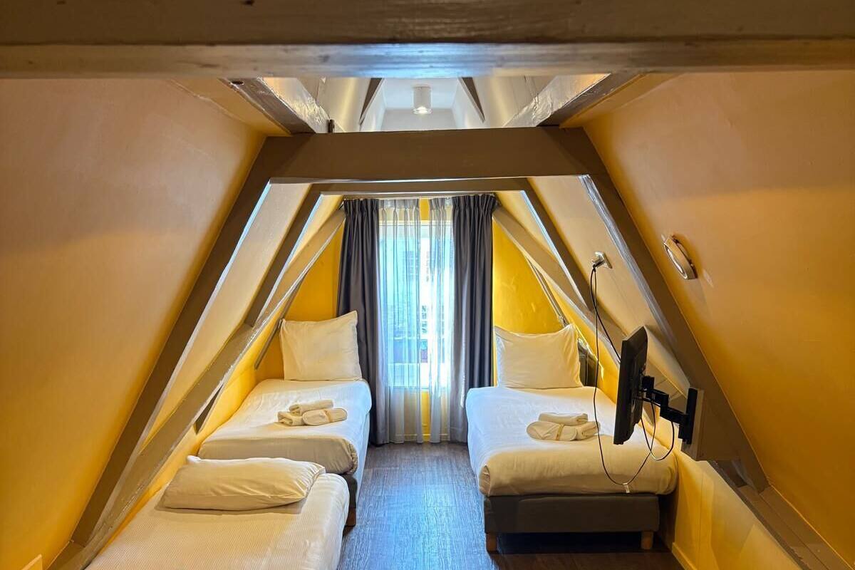 Una habitación con dos camas, un ventilador de techo y una ventana con cortinas.