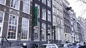 Un hotel con un letrero grande que dice 'HOTEL', múltiples ventanas y coches aparcados a lo largo de la calle.