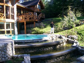 Una casa de madera con piscina de piedra y terraza de madera.
