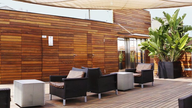 Una terraza de madera con mobiliario de mimbre y una planta grande.