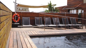 Una terraza de madera con sillones de descanso y una piscina.