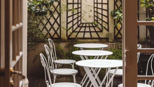 A wooden deck with white metal chairs and tables, surrounded by greenery and a decorative wall. - Hôtel Arvor Saint Georges (Paris)