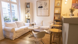 A modern living room with a white sofa, a small round table, and a rocking chair. There is a bookshelf with books and a framed picture on the wall. - Hôtel Arvor Saint Georges (Paris)